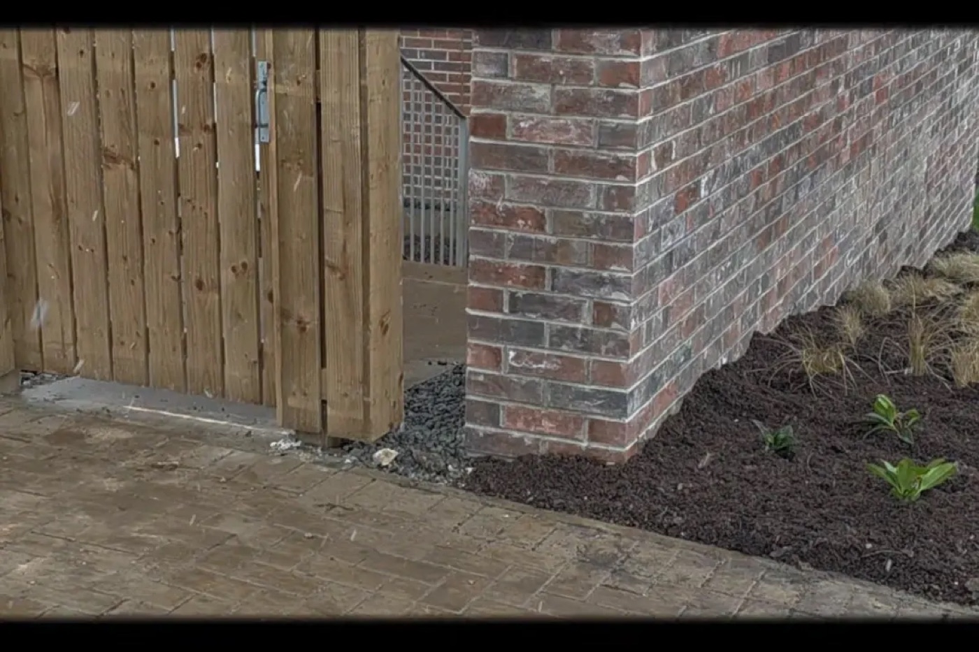 Brickwork at the corner of a new build home, with a timber gate, gravel and paving in front